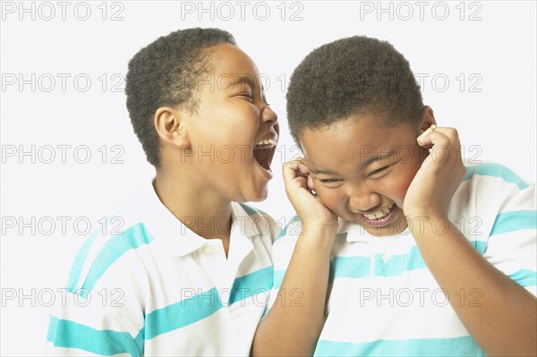 Young African boy yelling into twin brother's ear