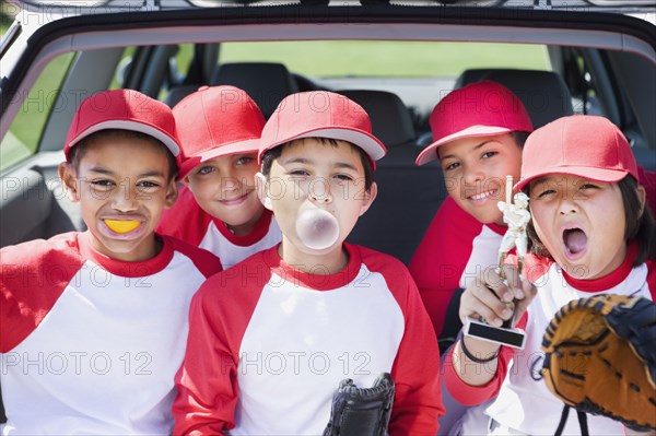 Multi-ethnic boys in baseball uniforms making faces and holding trophy