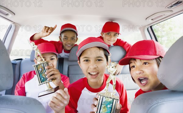 Multi-ethnic boys in car wearing baseball uniforms and holding trophies