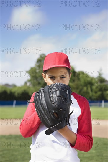 Mixed race boy in baseball uniform holding glove and concentrating