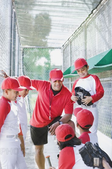 Multi-ethnic boys in baseball uniforms with coach in dugout