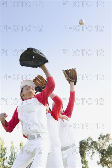 Multi-ethnic boys in baseball uniforms jumping to catch baseball