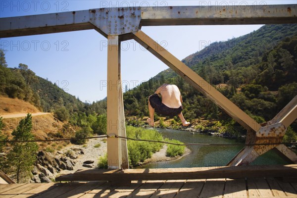 Caucasian man jumping into river from bridge