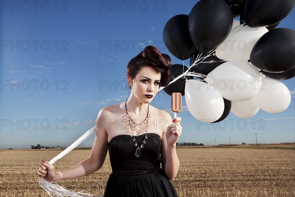 Glamorous woman holding balloons and eating popsicle