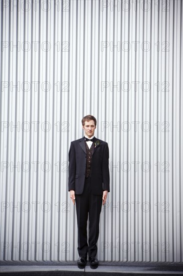 Serious groom standing near wall