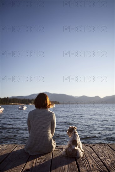 Woman and miniature schnauzer sitting on pier