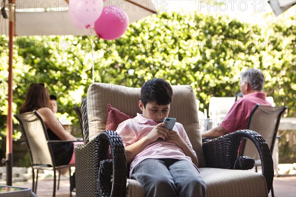 Bored boy using cell phone at party