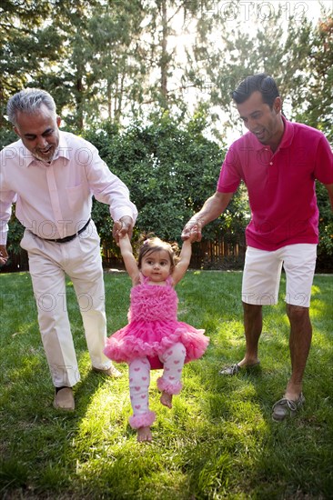 Father and grandfather helping daughter walk in backyard