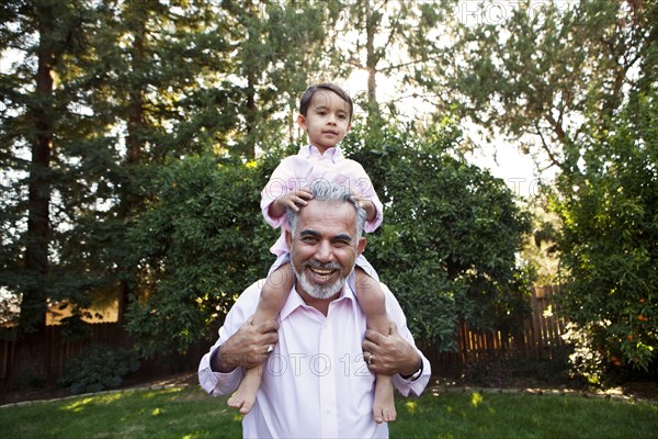 Grandfather carrying grandson on shoulders in backyard