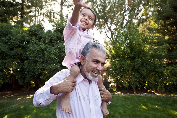 Grandfather carrying grandson on shoulders in backyard