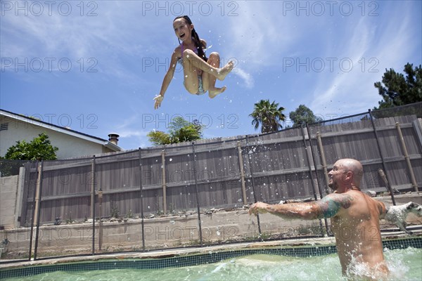 Caucasian father throwing daughter in backyard swimming pool