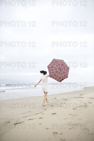 Woman walking in wind with umbrella on beach