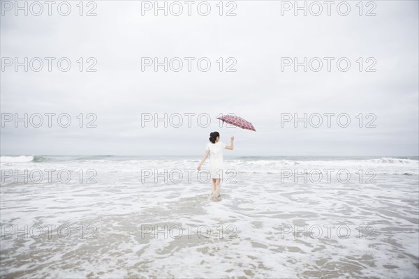 Woman wading with umbrella on beach