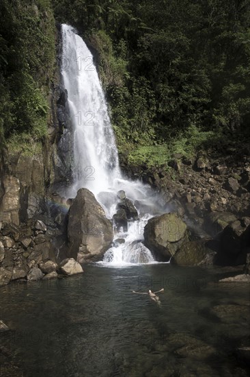 Mixed Race woman swimming in waterfall pool