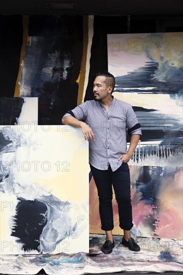 Pacific Islander artist leaning on paintings