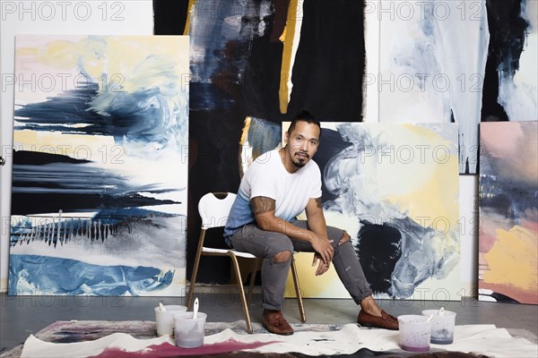 Pacific Islander artist sitting with paintings