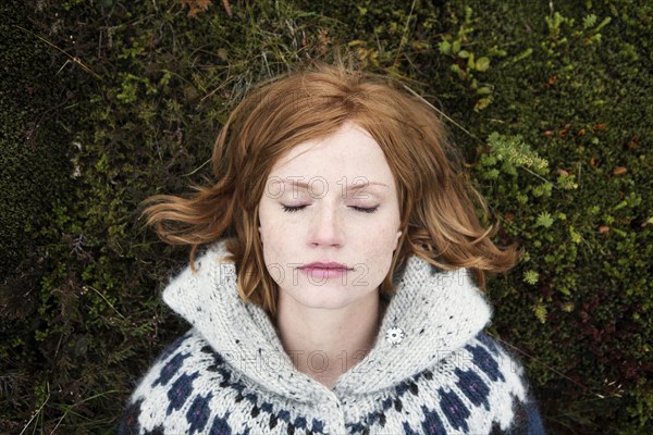 Caucasian woman laying on moss with eyes closed