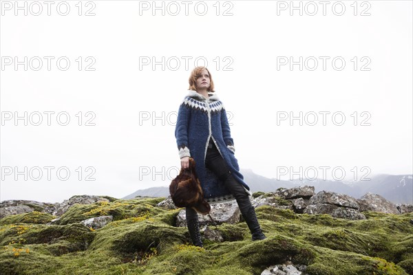 Caucasian woman standing on mossy rocks holding fur hat