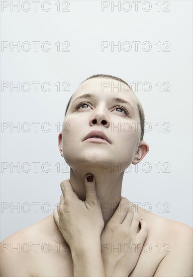 Caucasian woman with shaved-head holding neck with hands
