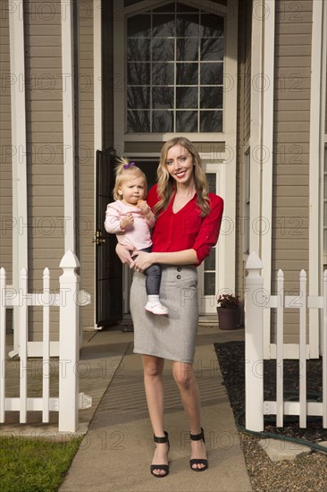 Caucasian mother posing near house with baby daughter