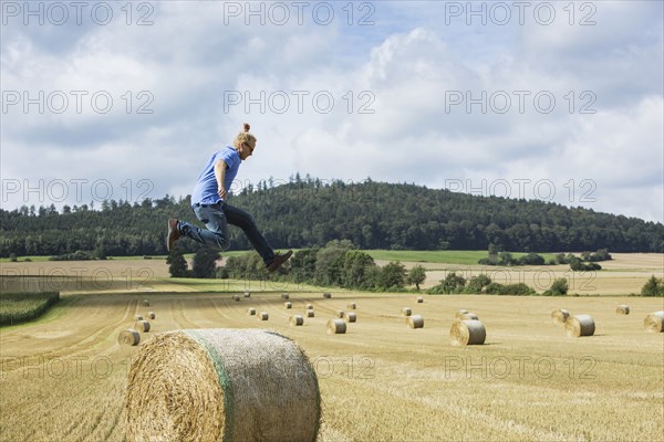 Farmer jumping over hay bale in field