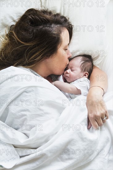 High angle view of mother kissing baby in bed