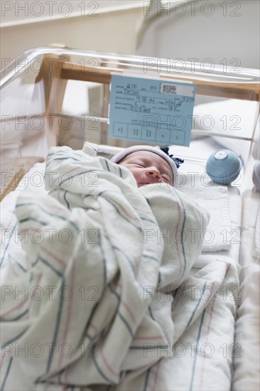 Mixed race wrapped in blanket in hospital crib