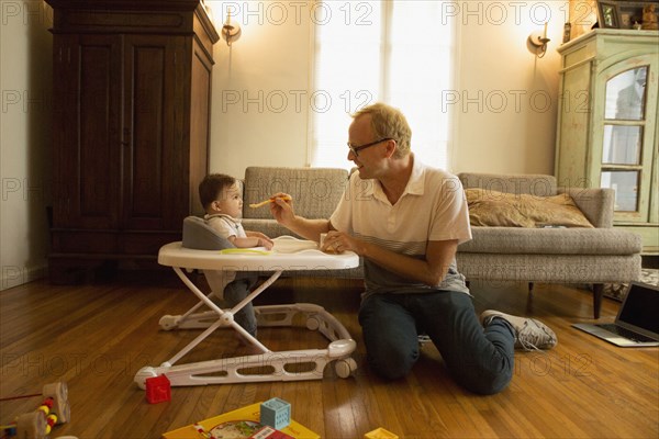 Father feeding son in high chair in living room