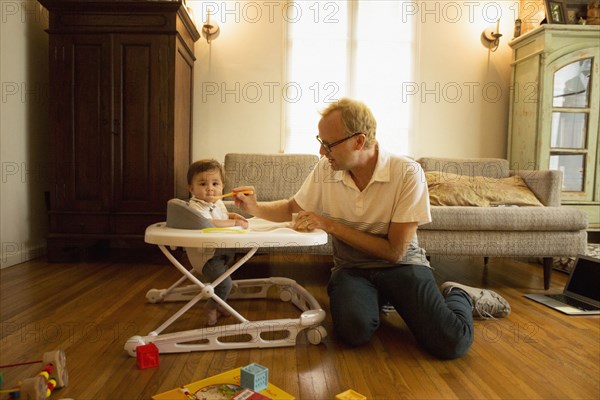 Father feeding son in high chair in living room