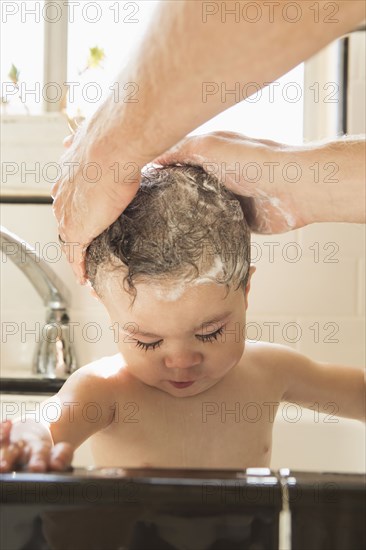 Father washing baby son in kitchen sink