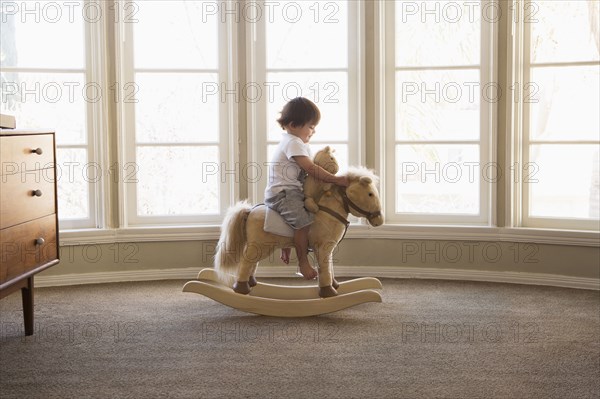 Mixed Race boy sitting on rocking horse near window