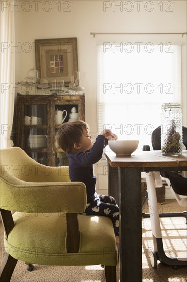 Mixed Race boy sitting at table eating from high bowl