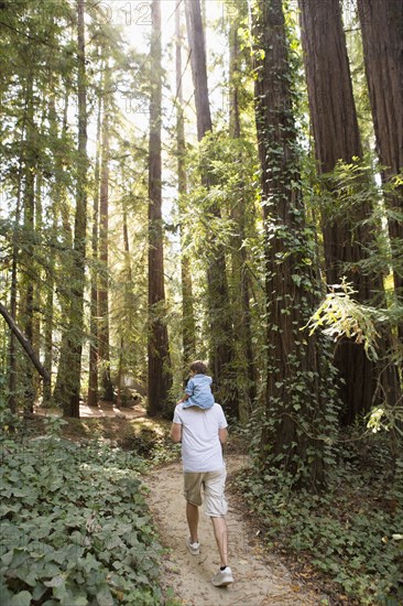 Father carrying son on shoulders on forest path