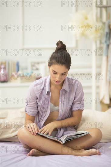 Caucasian woman reading magazine on bed