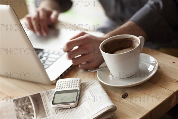 Close up of man using laptop with cup of coffee in cafe