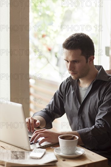 Man using laptop with cup of coffee in cafe