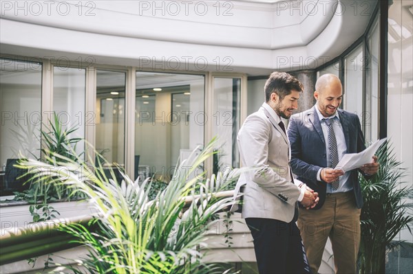 Caucasian businessmen reading paperwork on office balcony