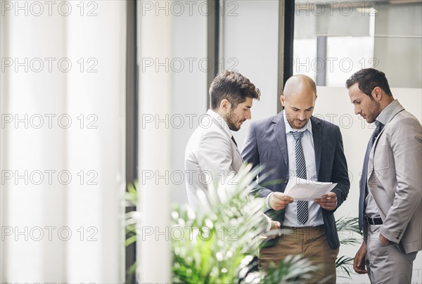 Caucasian businessmen reading paperwork in office corridor