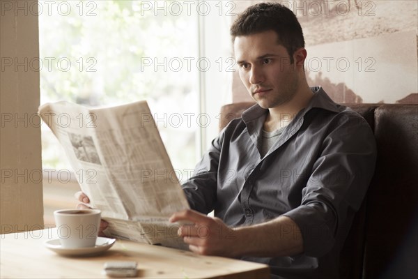 Man reading newspaper and drinking coffee in cafe
