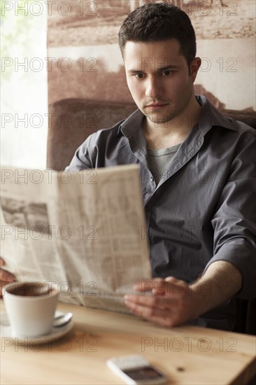 Man reading newspaper and drinking coffee in cafe