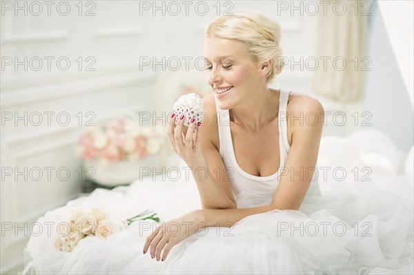 Smiling bride eating cupcake on bed