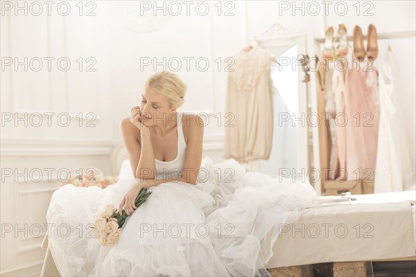 Pensive bride sitting with bouquet on bed