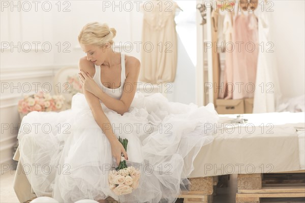 Pensive bride sitting with bouquet on bed