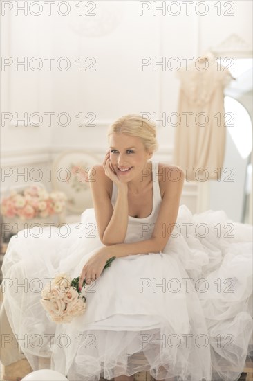 Smiling bride sitting with bouquet on bed