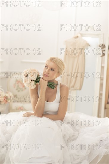 Bride sitting with bouquet on bed thinking