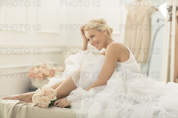 Smiling bride sitting with bouquet on bed