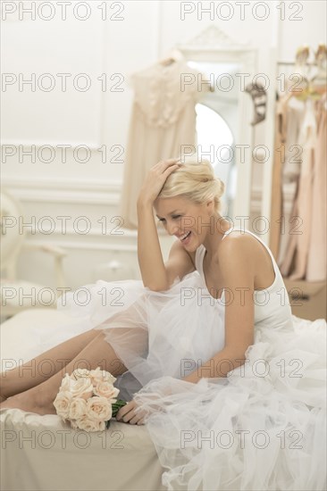Laughing bride sitting with bouquet on bed