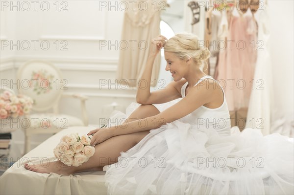 Smiling bride sitting with bouquet on bed