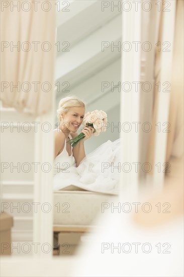 Smiling bride admiring herself in mirror on bed