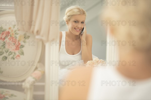 Smiling bride talking on cell phone in mirror